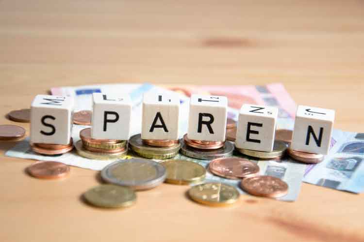 Die Wortwürfel "SPAREN" stehen auf Stapeln von Euro-Münzen, darunter ein Euro-Schein.